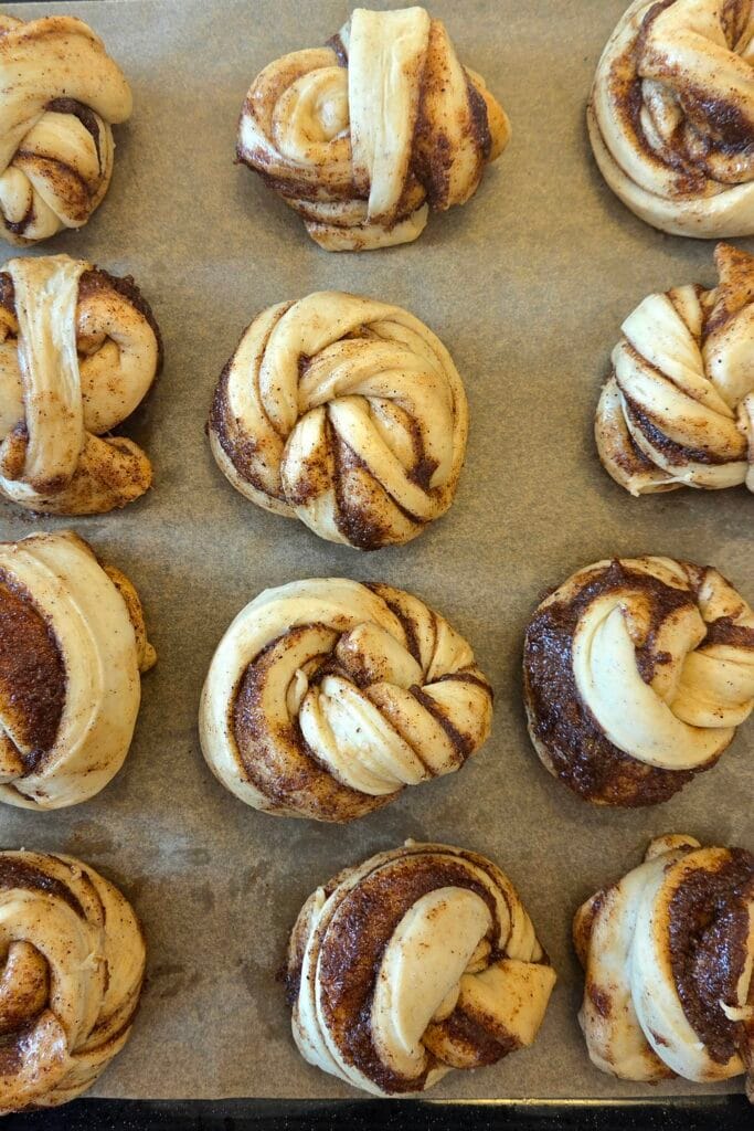 Shaped cinnamon knots proofing on a parchment-lined baking sheet before baking