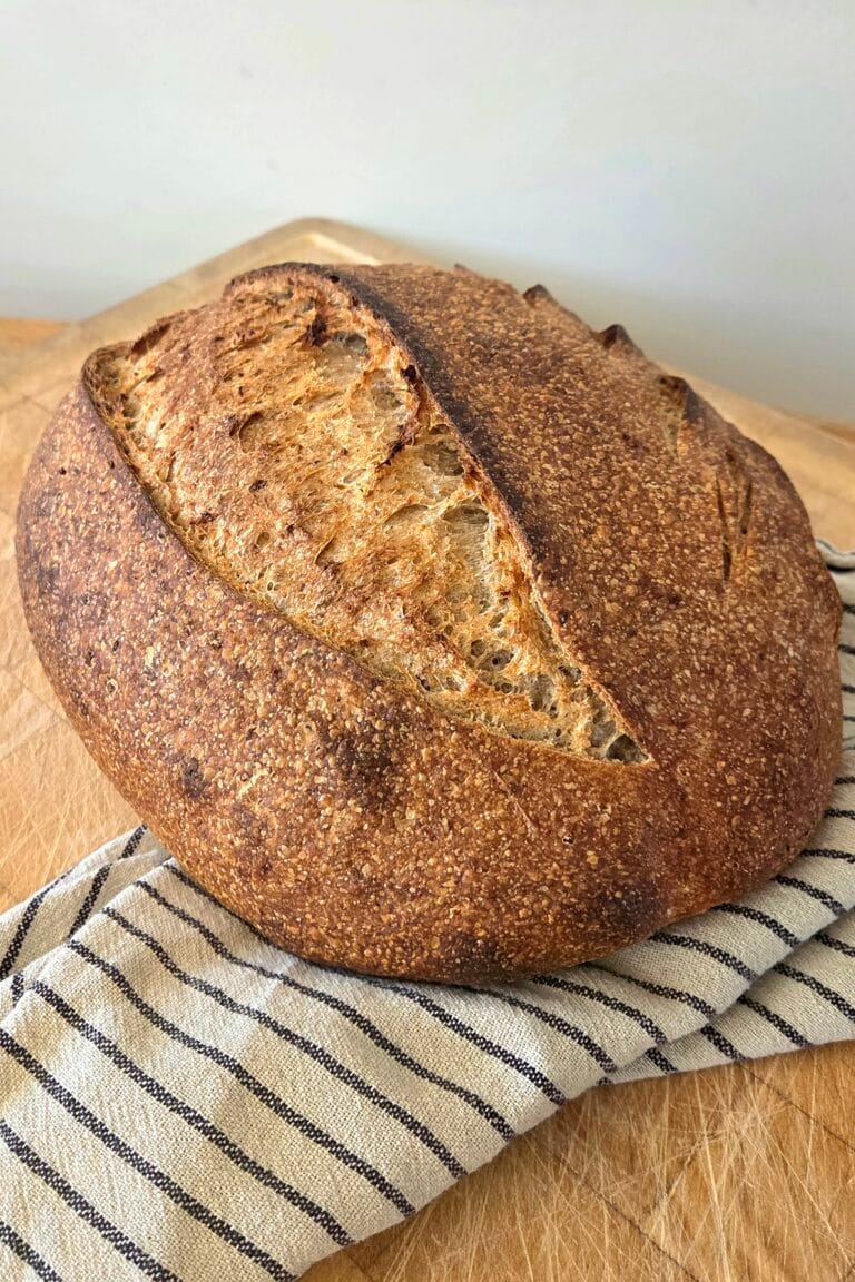 Oat sourdough bread with a scored, flour-dusted crust and a deep golden ear on a wooden board