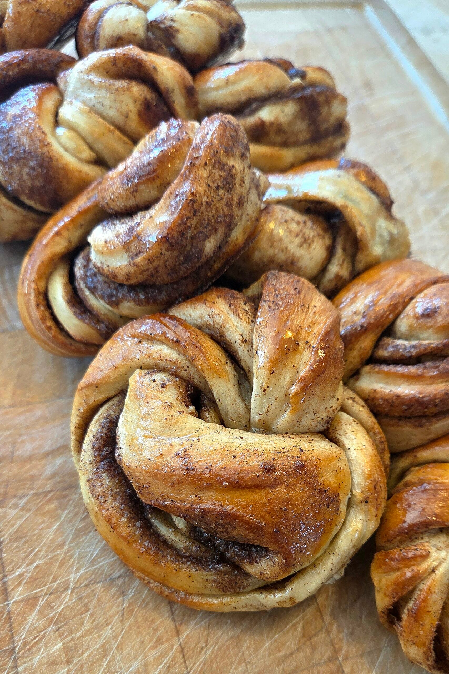 Glazed cinnamon knots with cardamom on a wooden board, brushed with sugar syrup