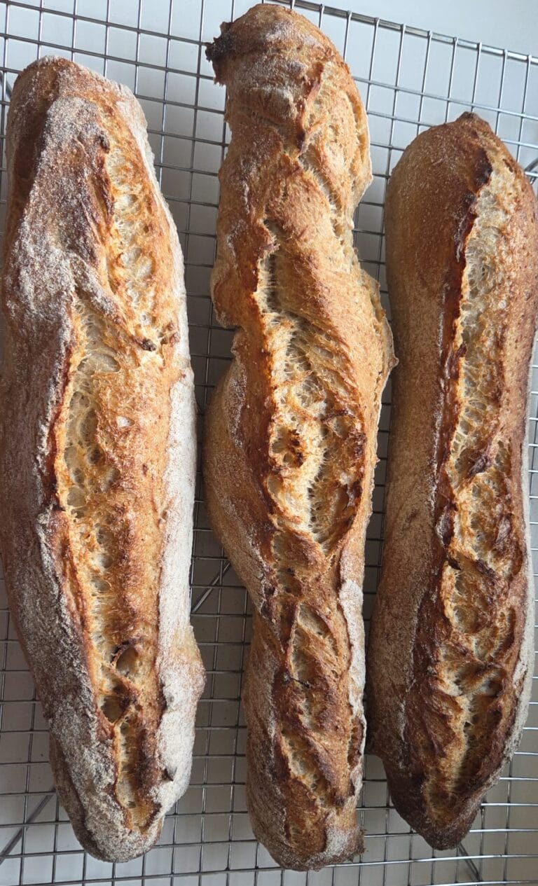 Crusty sourdough baguettes with a scored ear, cooling on a wire rack