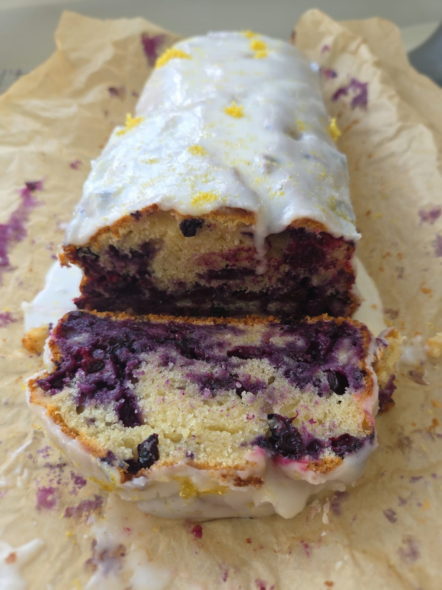 Sourdough discard blueberry loaf with thick white lemon glaze running down the sides, topped with lemon zest