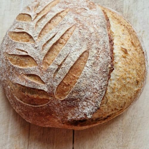 Scored whole grain sourdough bread with a golden, flour-dusted crust on a wooden board