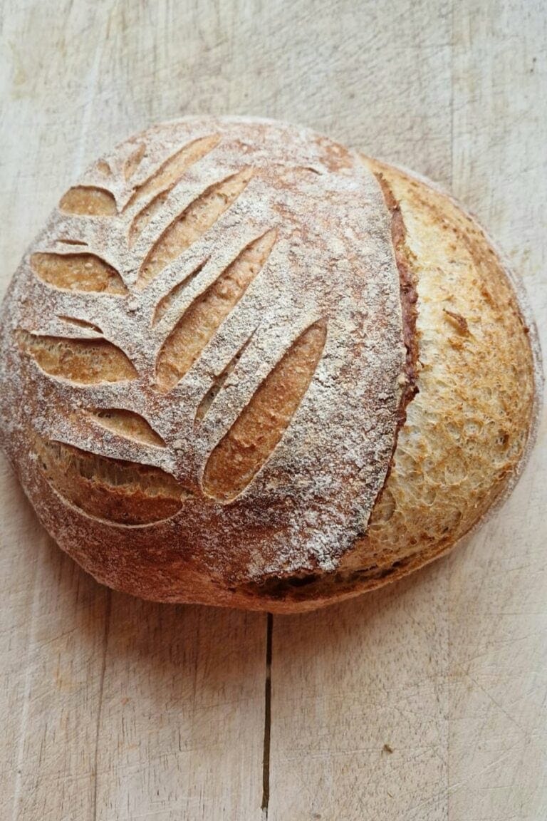 Scored whole grain sourdough bread with a golden, flour-dusted crust on a wooden board