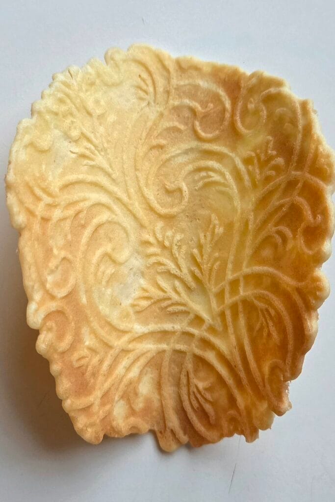 Flat krumkake showing the detailed rosemaling pattern before rolling