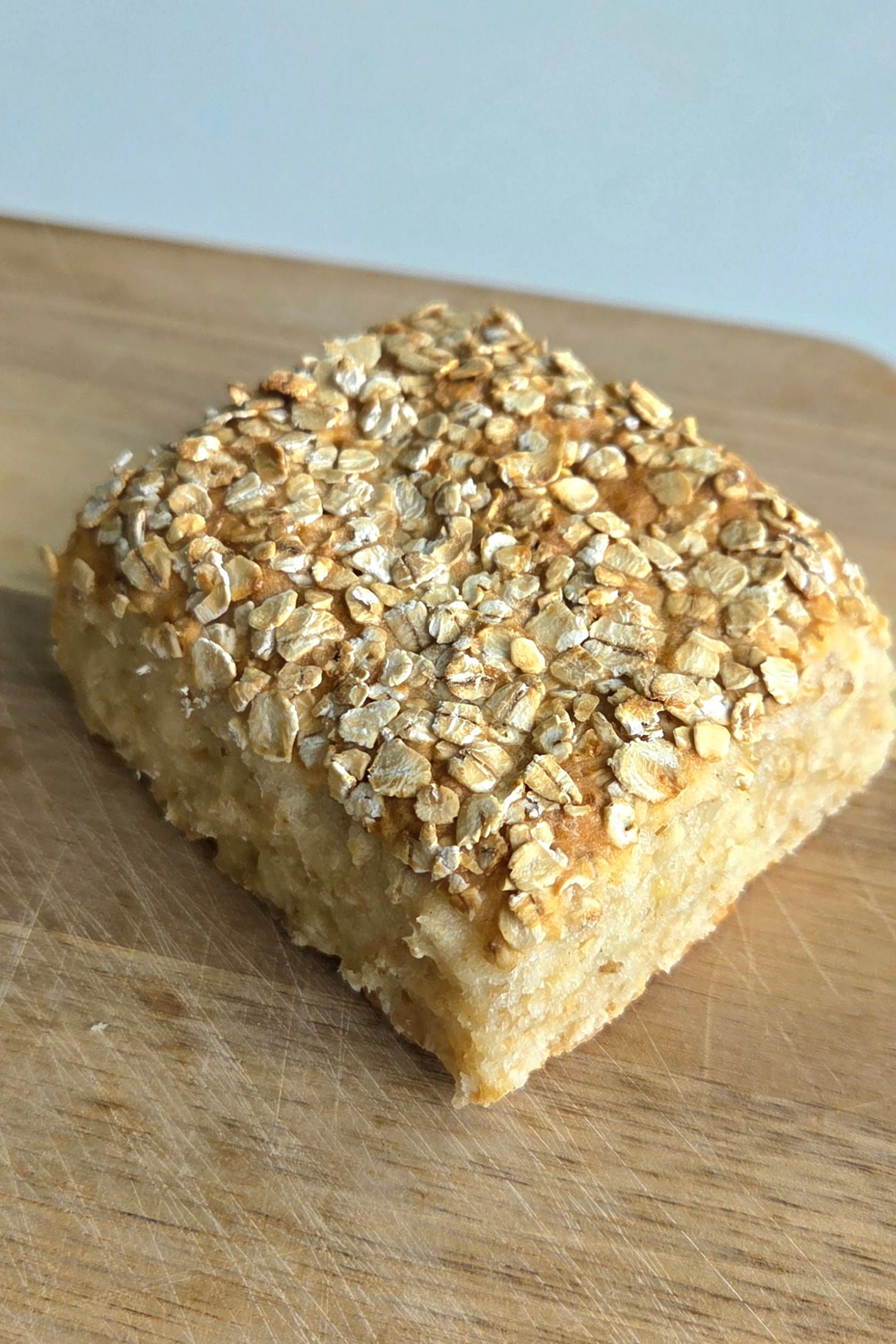 Oat scones baked as one tray and torn into squares, topped with rolled oats on a wooden board