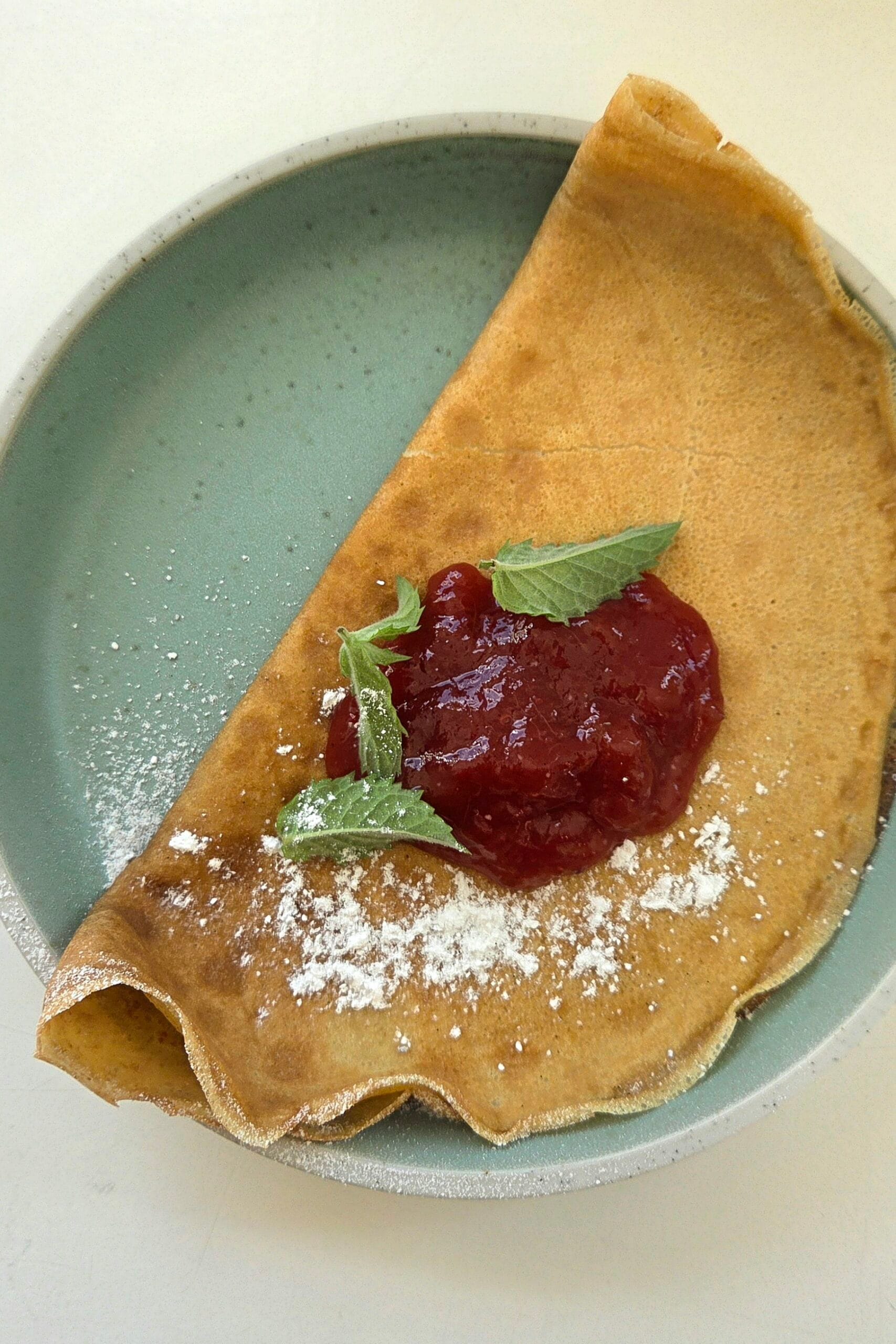 Thin sourdough discard pancakes stacked on a plate, folded and dusted with powdered sugar