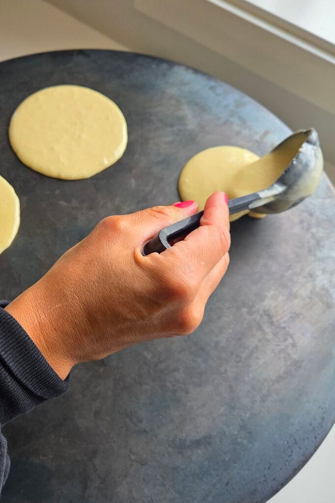 Ladling svele batter onto a hot Norwegian takke griddle in even rounds