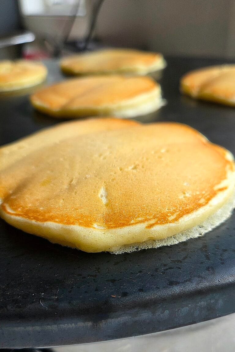 Norwegian sveler cooking on a black cast iron griddle, golden and puffed at the edges