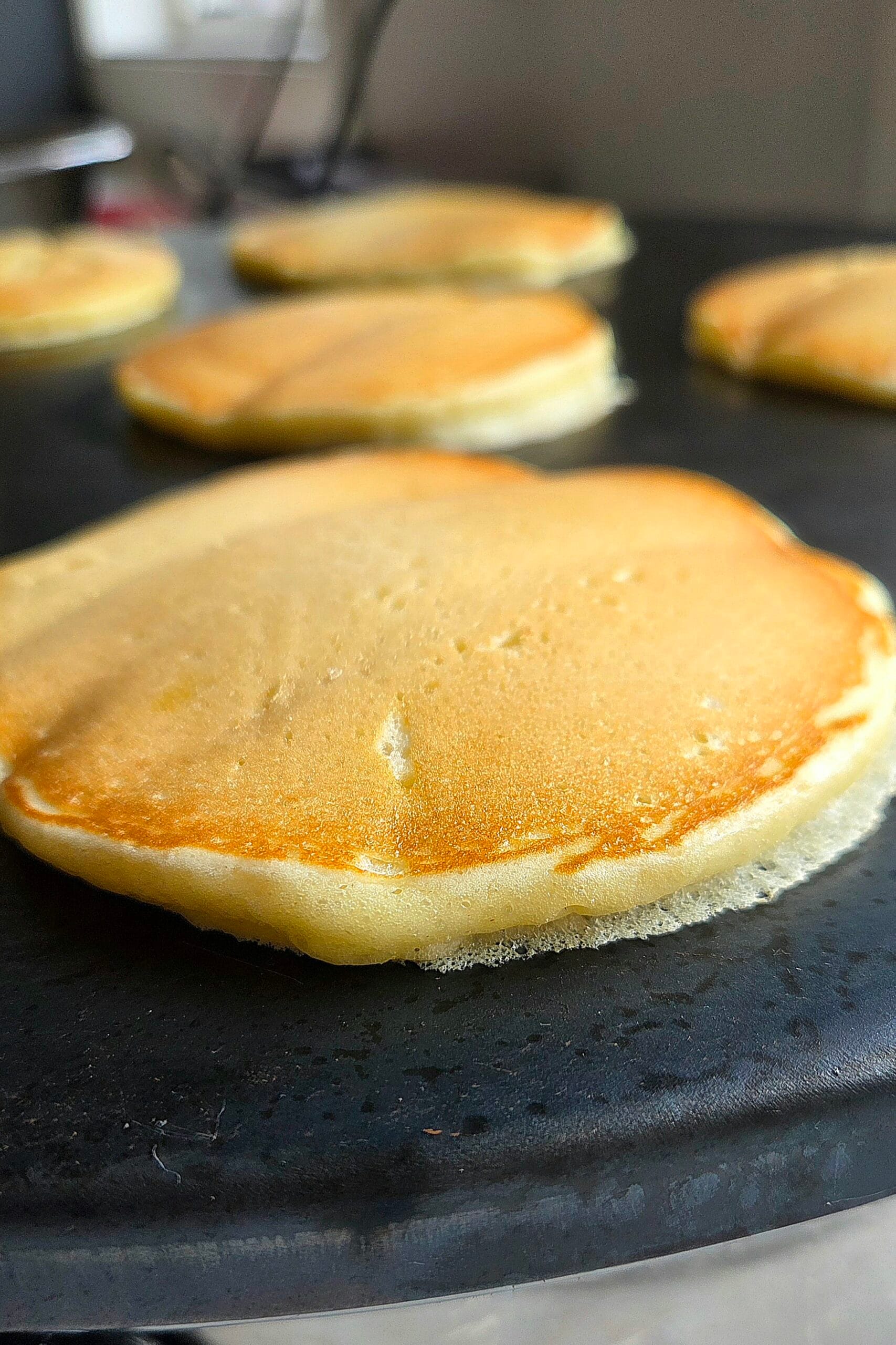 Norwegian sveler cooking on a black cast iron griddle, golden and puffed at the edges