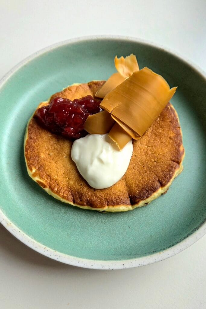 A Norwegian svele on a green plate with raspberry jam, sour cream and brown cheese