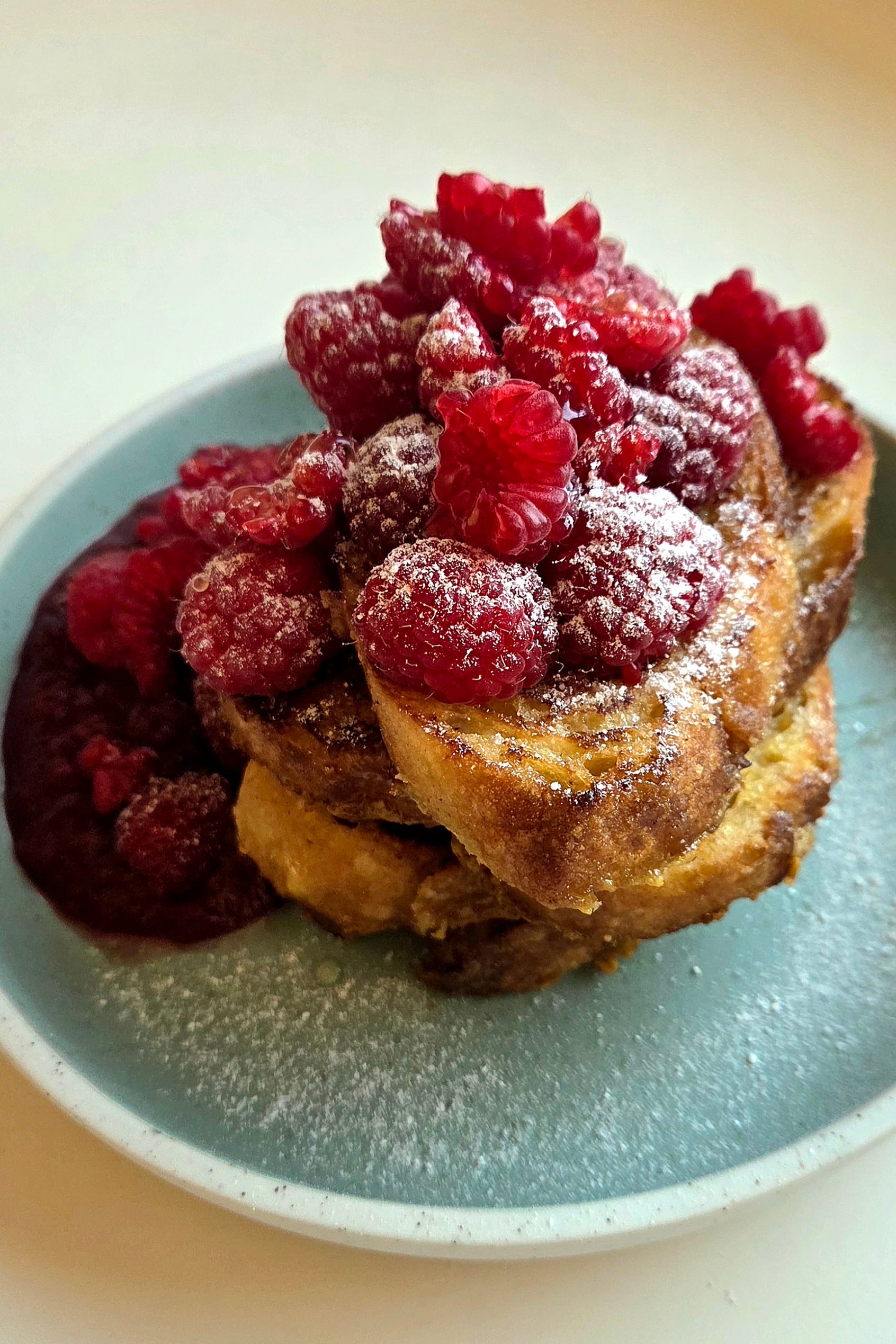 Norwegian French toast (arme riddere) made with sourdough, stacked on a green plate with fresh raspberries and powdered sugar