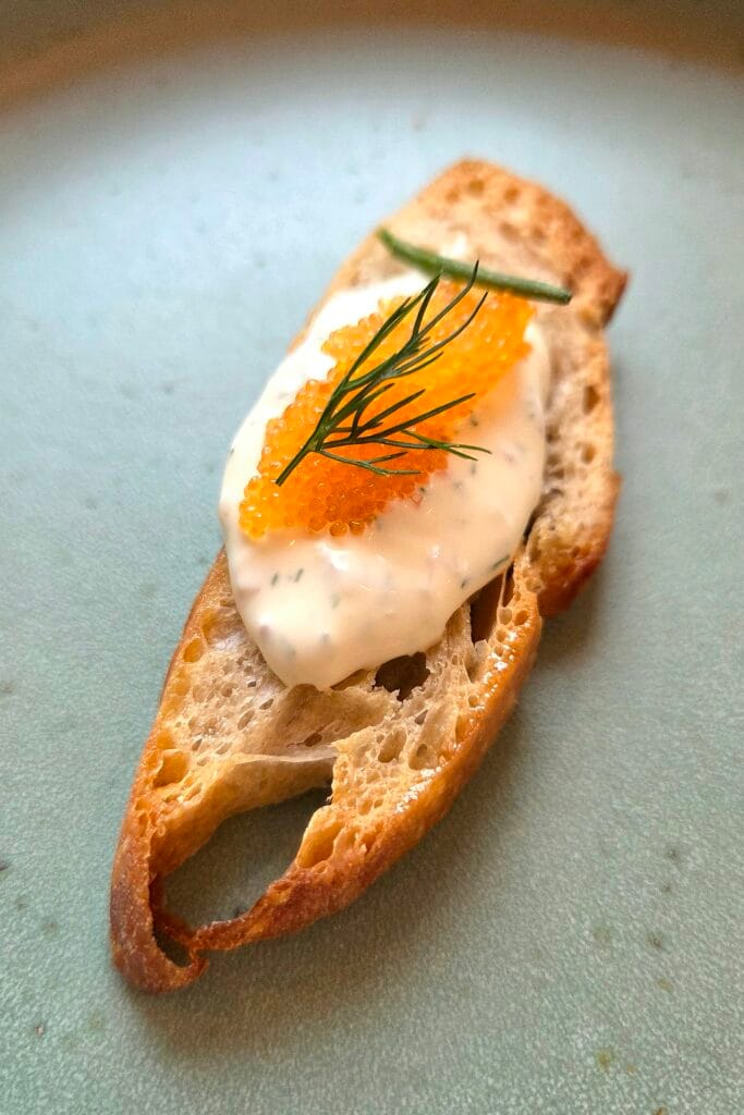 A sourdough chip topped with dill cream, roe and fresh dill