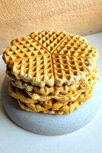 Stack of golden sourdough waffles in the Norwegian heart shape on a grey speckled plate