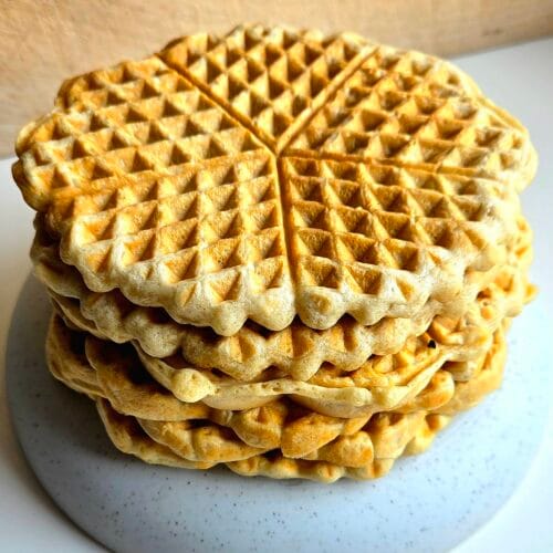 Stack of golden sourdough waffles in the Norwegian heart shape on a grey speckled plate