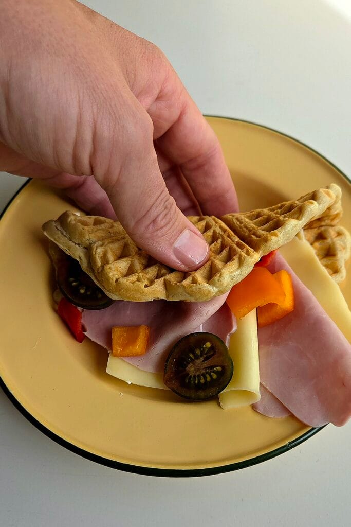 Soft sourdough waffle folded around ham, cheese and tomato on a yellow plate