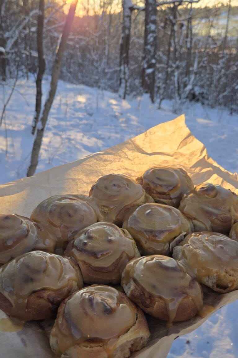Cardamom cinnamon rolls with cream cheese frosting in a baking pan, one roll pulled apart to show the spiral