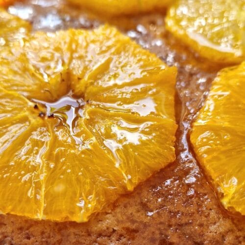 Moist orange cake topped with glossy glazed orange slices, cooling on a wire rack
