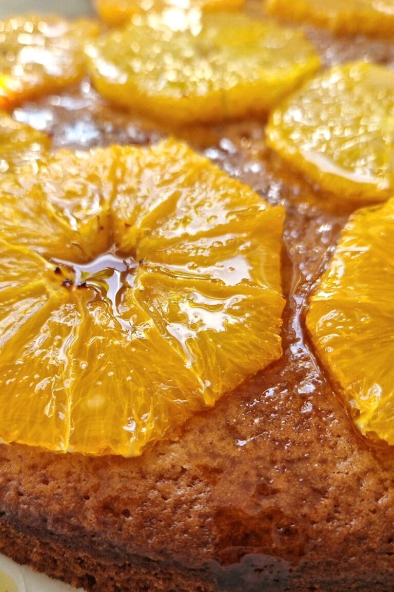 Close-up of a moist orange cake with glossy syrup-soaked orange slices arranged on top