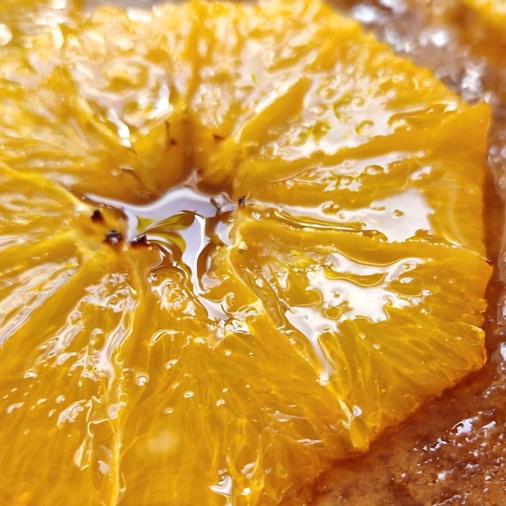 Close-up of a baked orange slice glazed with warm orange syrup, caramelized at the center, on top of a moist orange cake