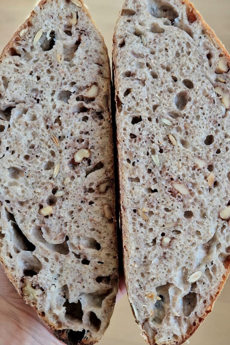 Walnut sourdough bread sliced open on a wooden board, showing walnuts through the open crumb