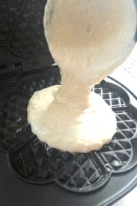 Sourdough waffle batter being poured onto a hot buttered heart-shaped waffle iron