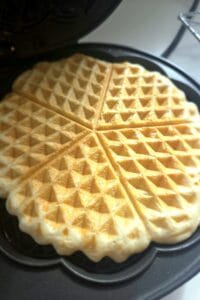 Golden sourdough waffle in an open heart-shaped waffle iron, cooked and ready to lift out