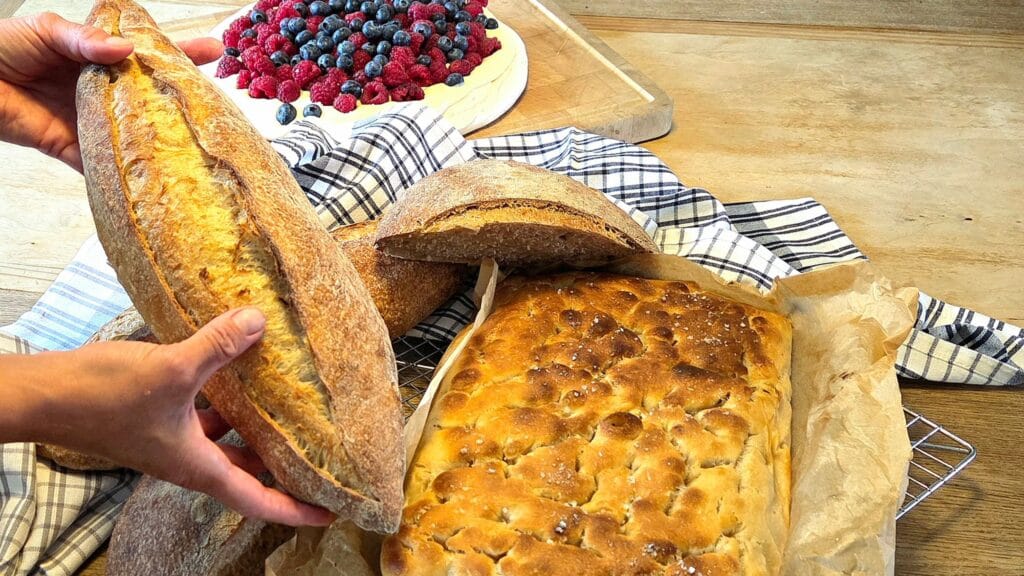 Freshly baked sourdough loaves, baguette and focaccia on a wooden table