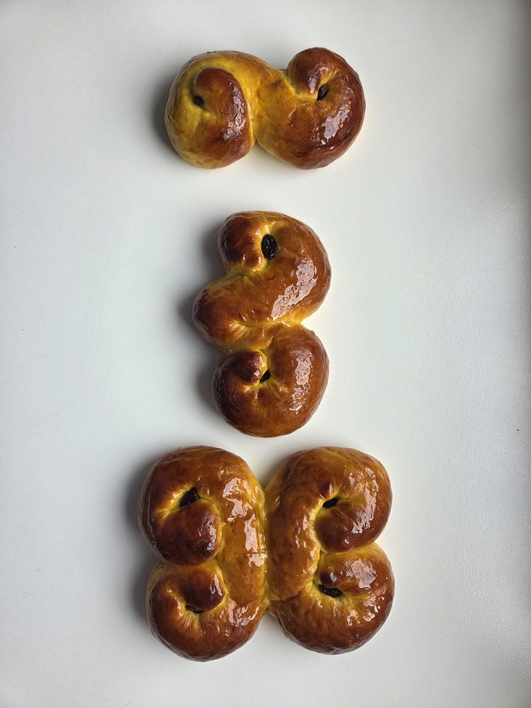 Lussekatter shaped in classic Swedish forms — the S-curl julgalt and the double golden wagon, before baking