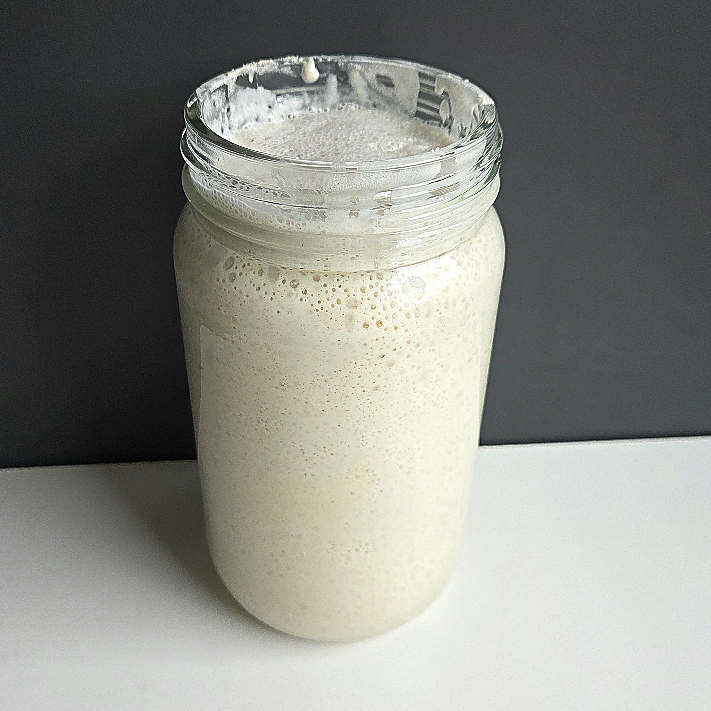 Sourdough starter rising in a jar, bubbles climbing up the sides