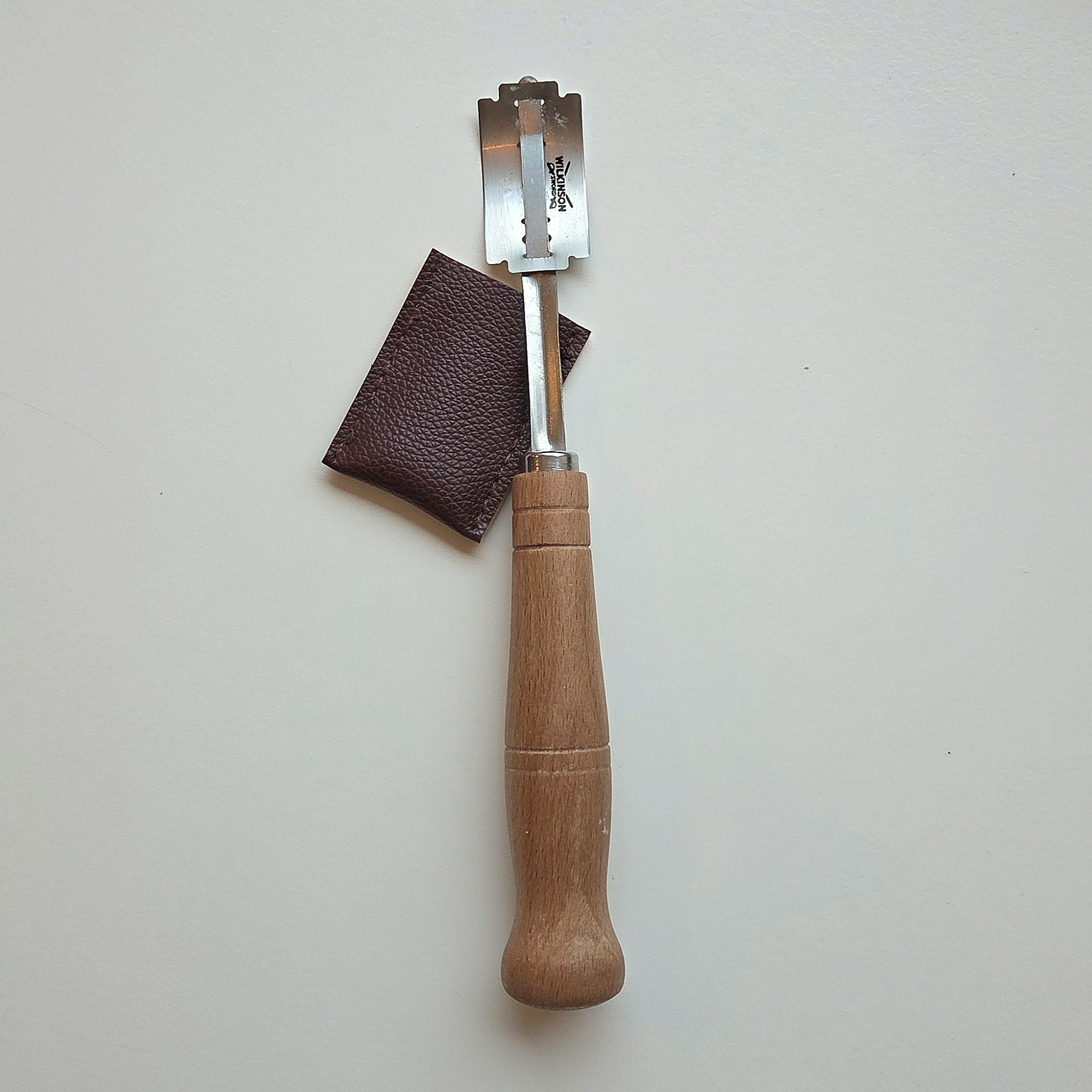 Bread lame for scoring sourdough — a double-edged razor blade mounted on a metal handle, with its leather blade cover
