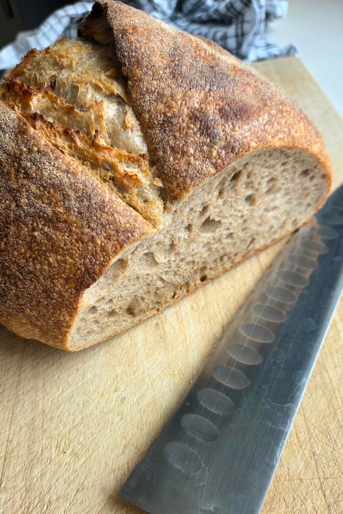 A cut sourdough loaf on a wooden board with a bread knife