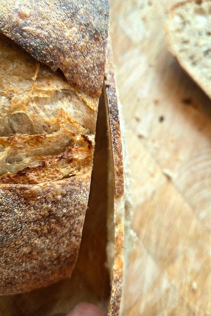 Cutting a paper-thin slice from a two-day-old sourdough loaf with a serrated knife