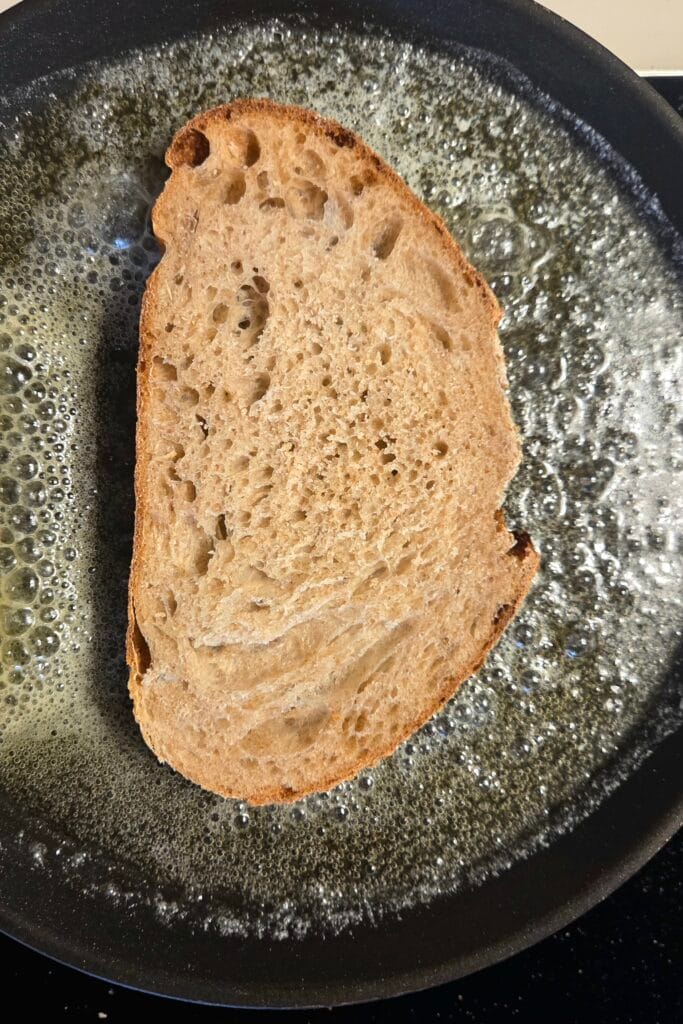 A slice of sourdough frying in foaming butter in a black skillet