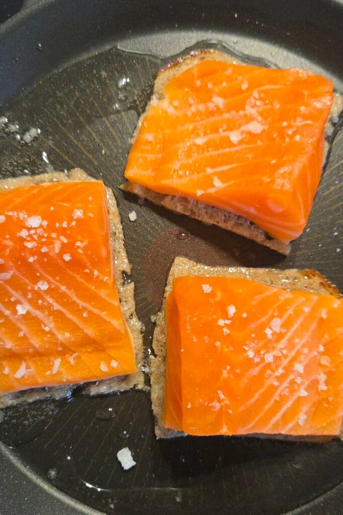 Sourdough-crusted salmon frying bread side down in a skillet over medium-low heat
