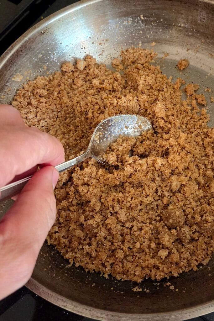 Buttered sourdough breadcrumbs frying golden in a pan, stirred with a spoon
