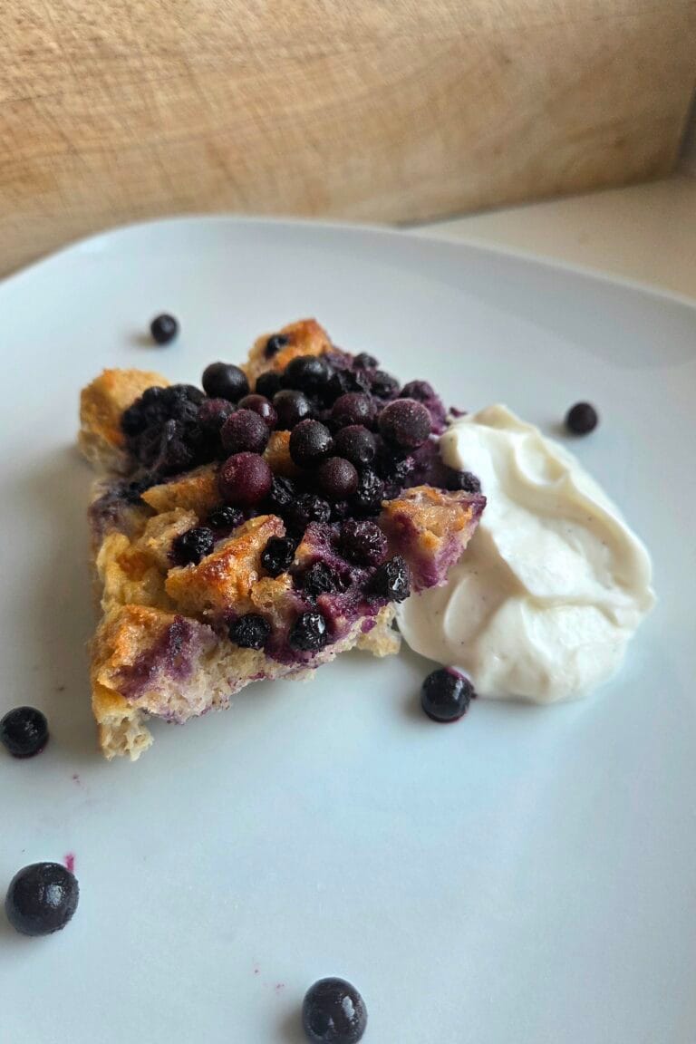 Square of sourdough bread pudding with blueberries and Greek vanilla yogurt on a white plate