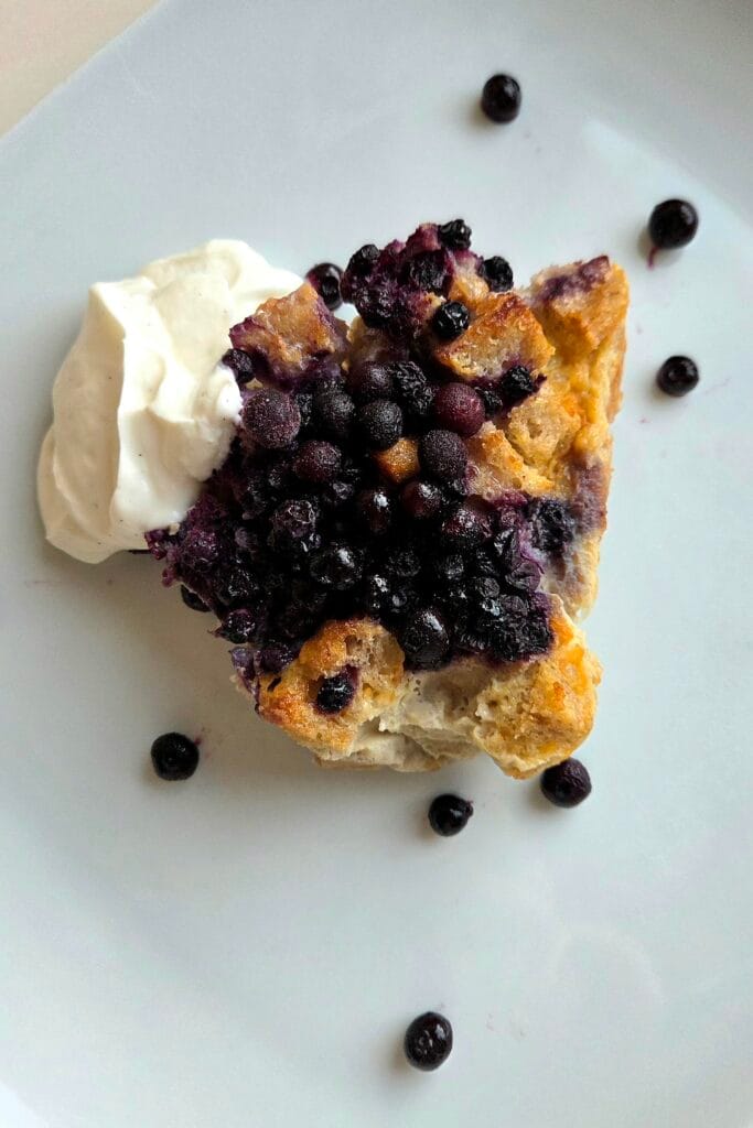 Square of sourdough bread pudding with blueberries and Greek vanilla yogurt on a white plate