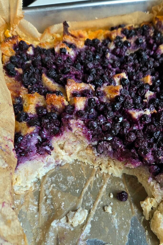 Slice of sourdough bread pudding showing distinct bread cubes set in vanilla custard under a blueberry layer