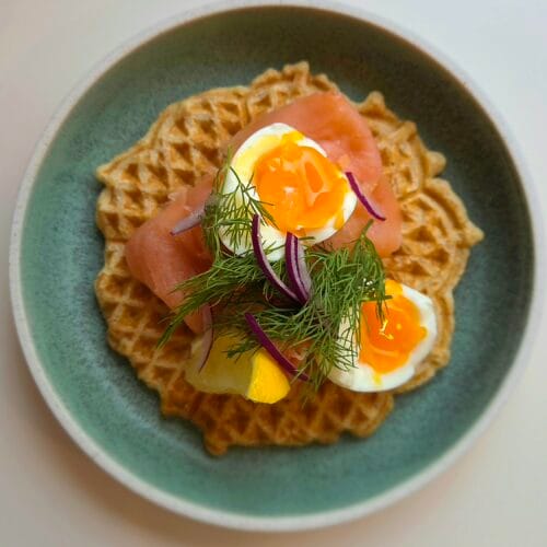 Savory waffles topped with smoked salmon, soft-boiled egg, dill and red onion on a green plate