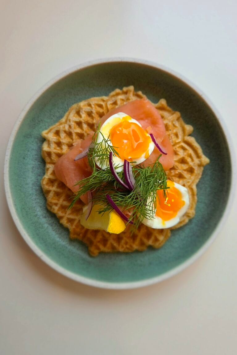 Savory waffles topped with smoked salmon, soft-boiled egg, dill and red onion on a green plate