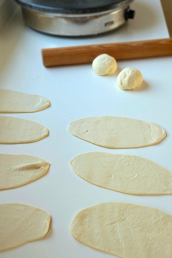 Rolled sourdough discard naan dough ovals on a bare, unfloured counter with a rolling pin