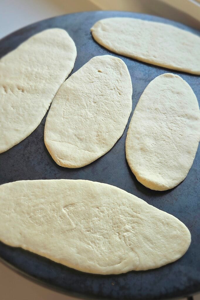 Raw sourdough discard naan dough ovals resting on a cast iron griddle