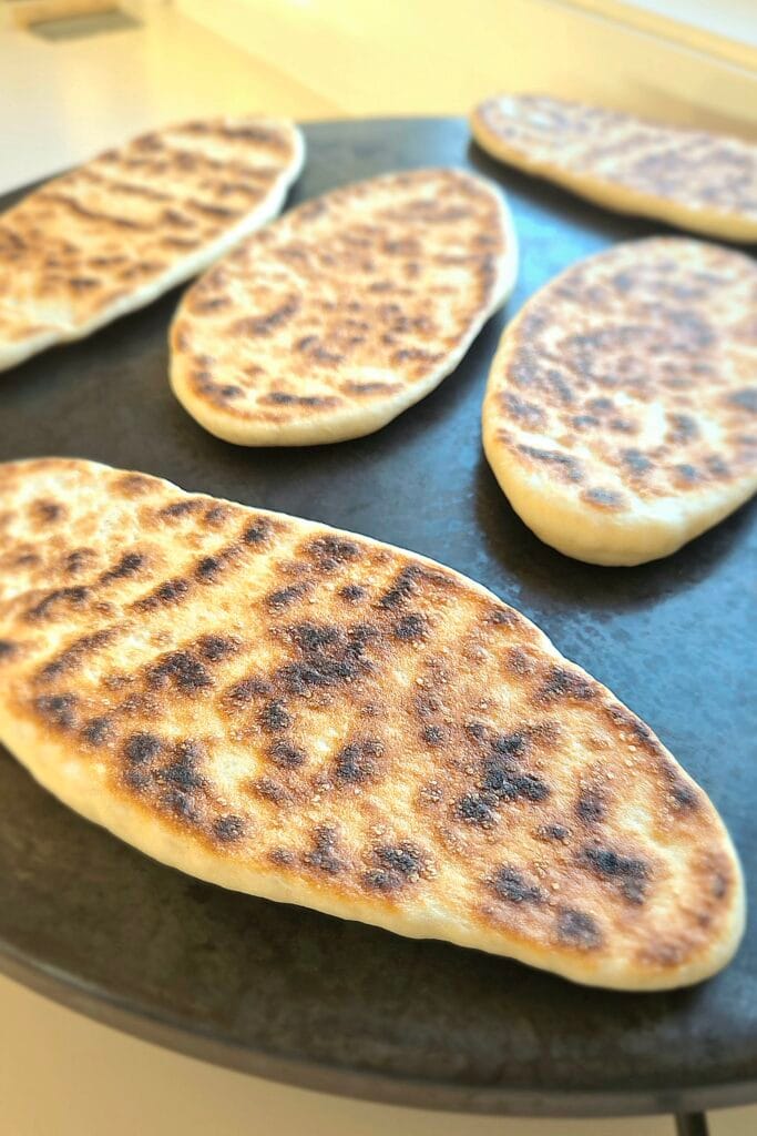 Sourdough discard naan cooking on a dry griddle with blistered golden spots