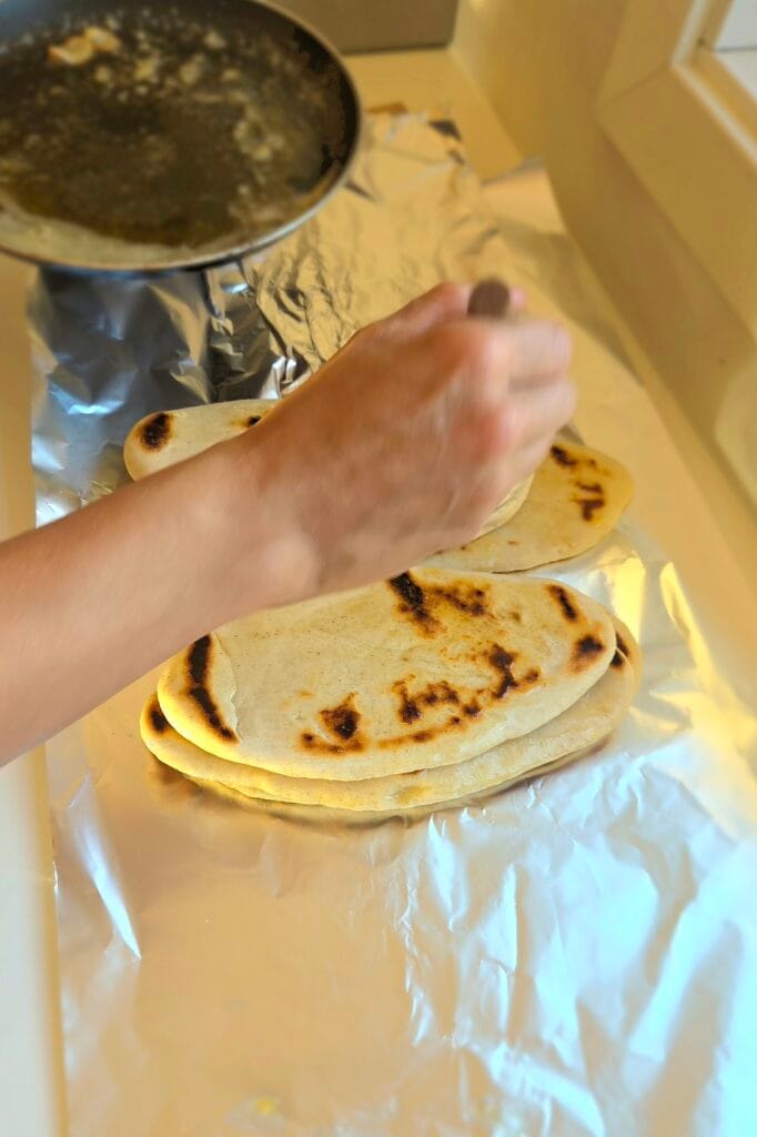 Garlic-cumin butter being brushed over hot sourdough discard naan straight from the griddle
