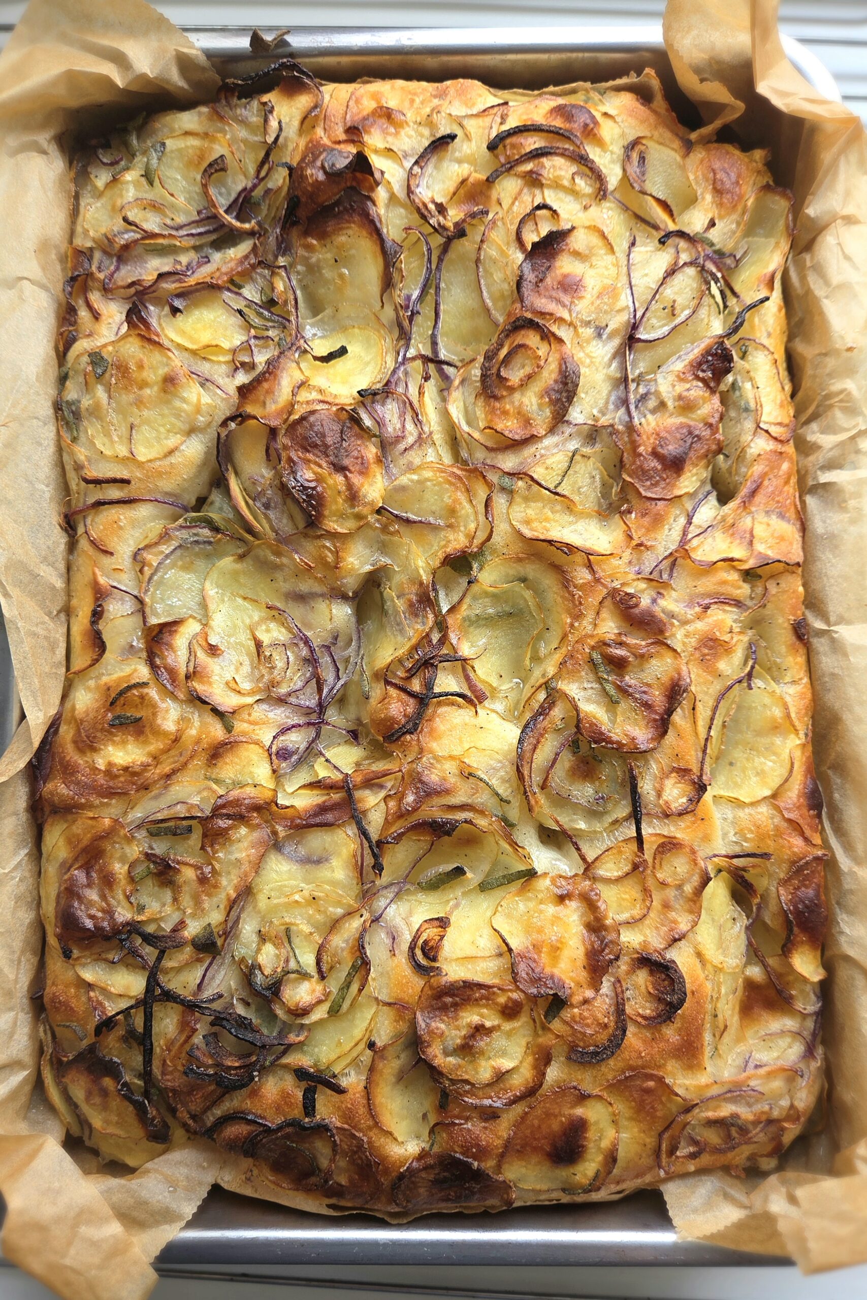 Potato focaccia baked in a rectangular pan with red onion and sage