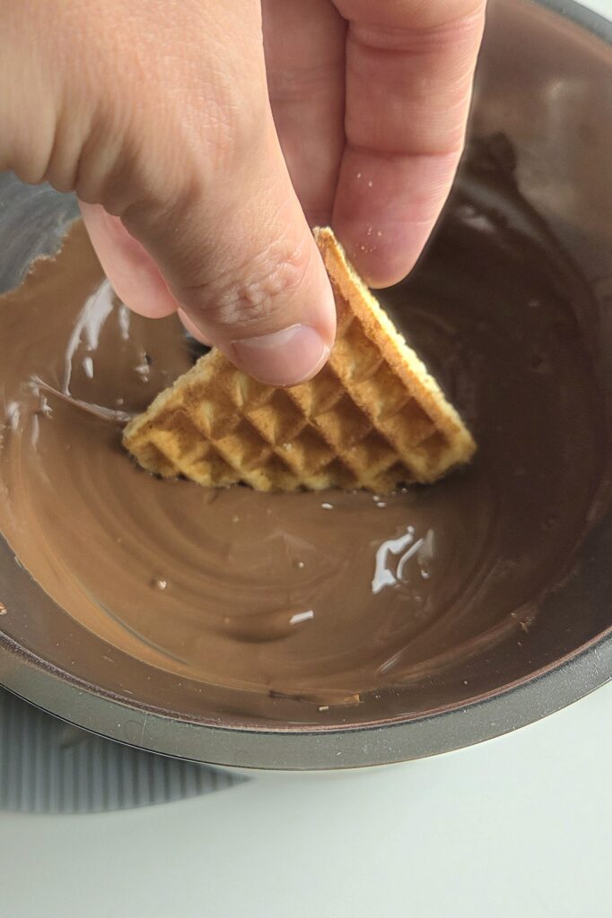 Dipping a crispy Norwegian waffle heart halfway into melted chocolate
