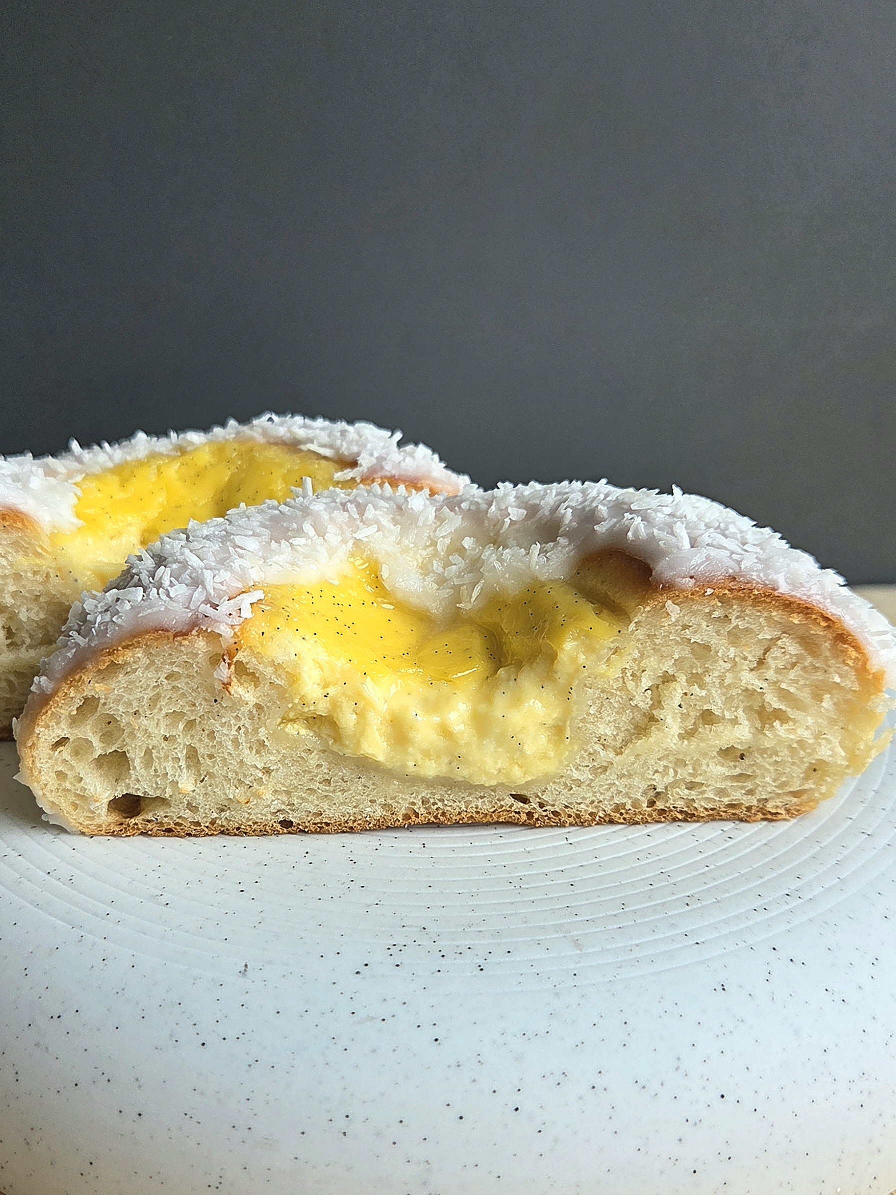 Skolebrød cut in half on a white plate, showing the soft cardamom crumb and vanilla custard filling under a coconut-covered glaze