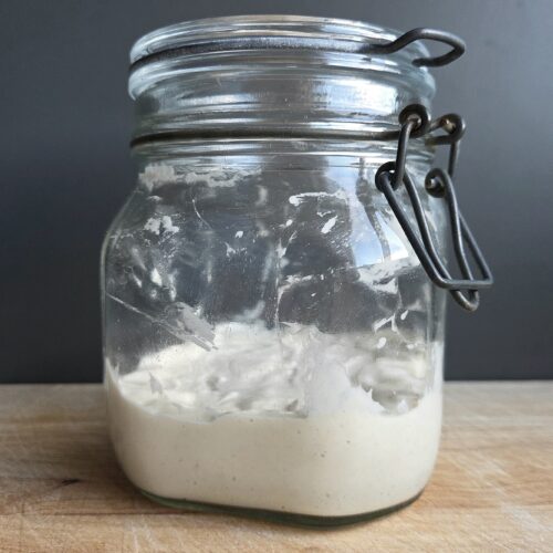 Homemade sourdough starter in a glass jar on a wooden board