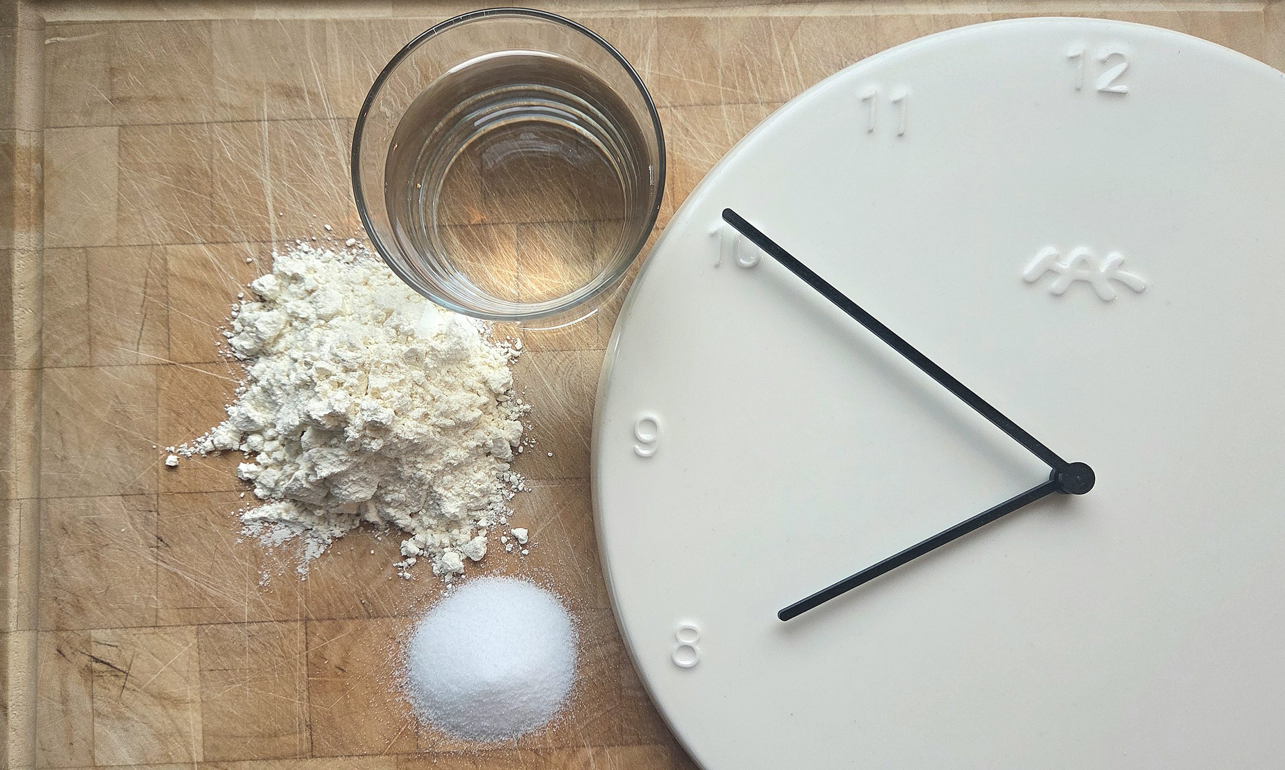 Flour, water, salt and a clock laid out on a wooden board — the four things that make sourdough