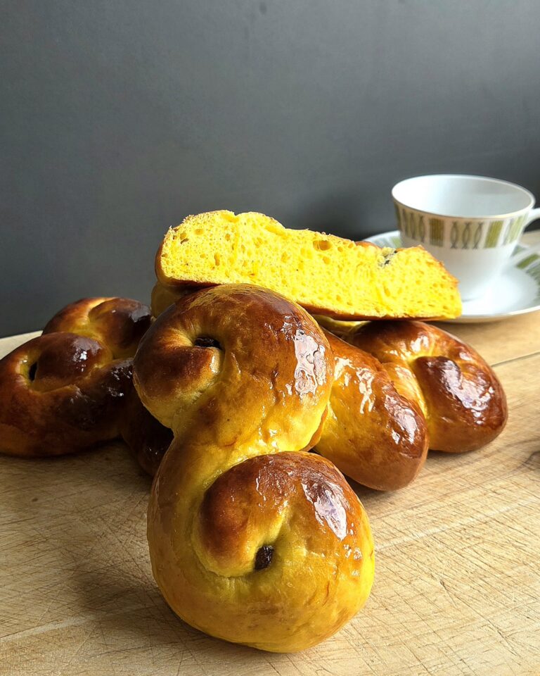Stacked lussekatter saffron buns with a cut slice showing the soft crumb, served with coffee